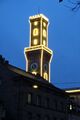 Gebäude <!--LINK'" 0:95--> dahinter beleuchteter Rathausturm bei Nacht im Dez. 2022 - die Beleuchtung des Rathauses sollte 1989 aus nicht mehr zeitgemäßen Gründen abgeschaltet werden unter der Bezeichnung "beleuchteter Mississippi Dampfer", was aber von der Bevölkerung abgelehnt wurde.